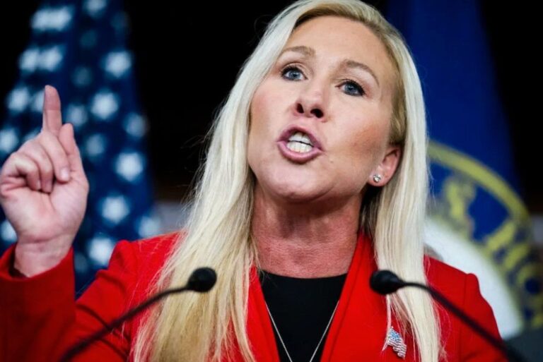 Marjorie Taylor Greene speaking into a microphone, media in the background